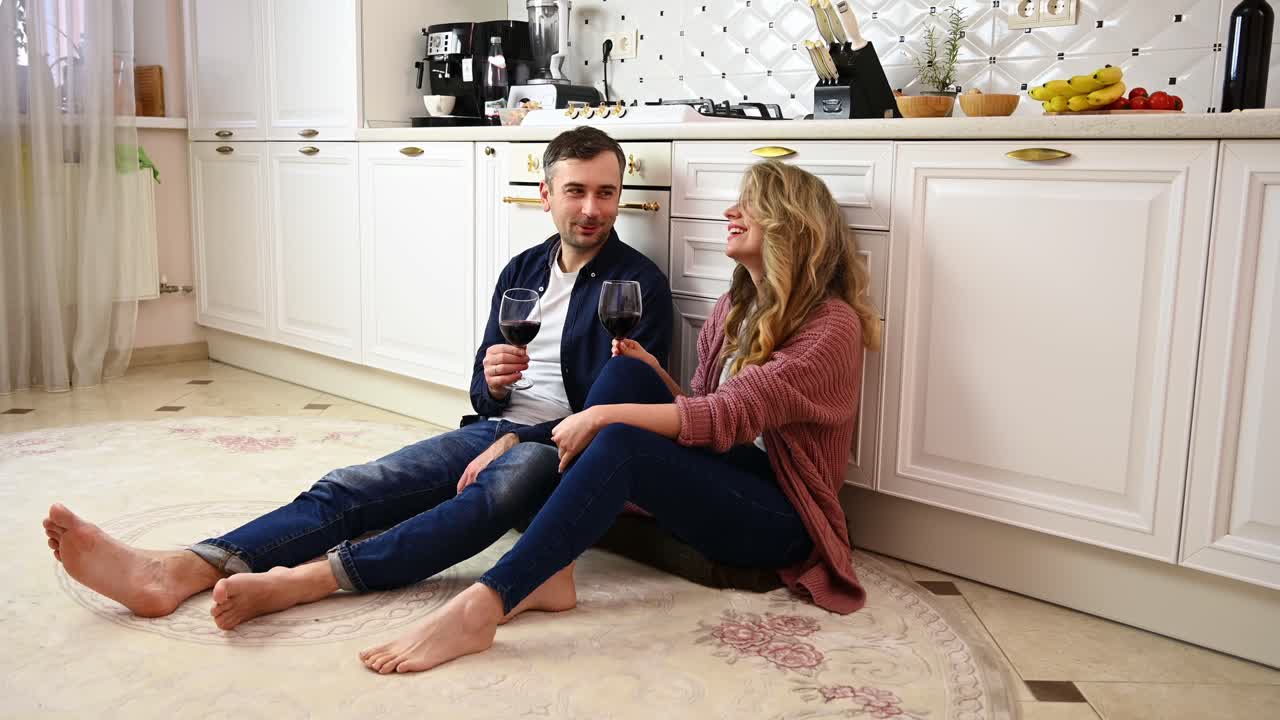 Young happy couple relaxing and talking on kitchen floor holding glasses with red wine. Valentines day. Relationships and feelings concept. Cinematic move