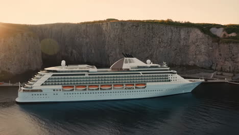 luxury cruise ship docked by a rocky cliff at sunrise or sunset