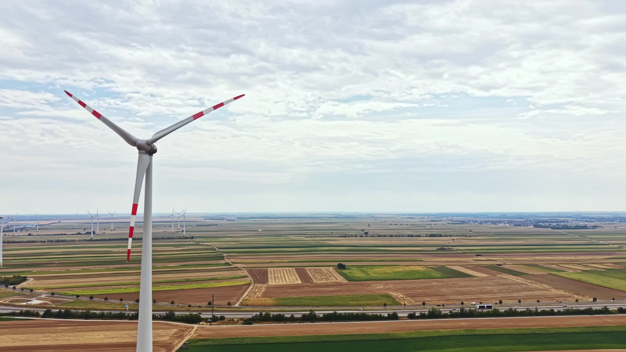 Wind turbine stands tall in a wide open field with rows of crops and patches of farmland under a cloudy sky in a rural area
