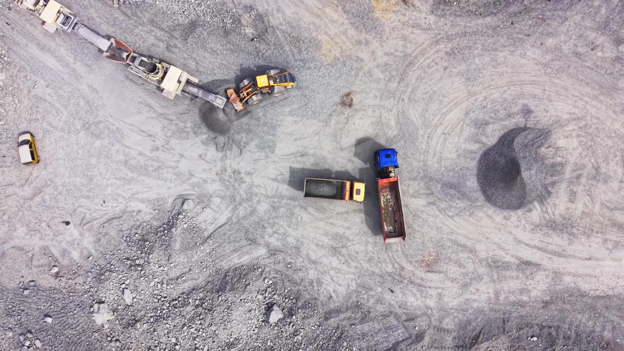 Trucks and loader in gravel quarry. Dump trucks, loader and conveyor amid gray gravel piles.