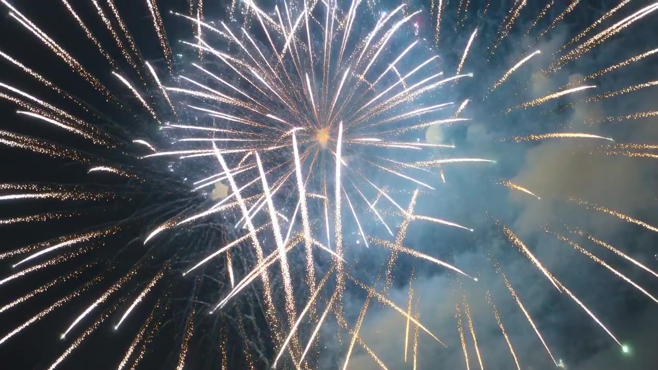 Lancio di razzi, con proiettili a crisantemo che esplodono nel cielo notturno durante uno spettacolo pubblico, con fumo.