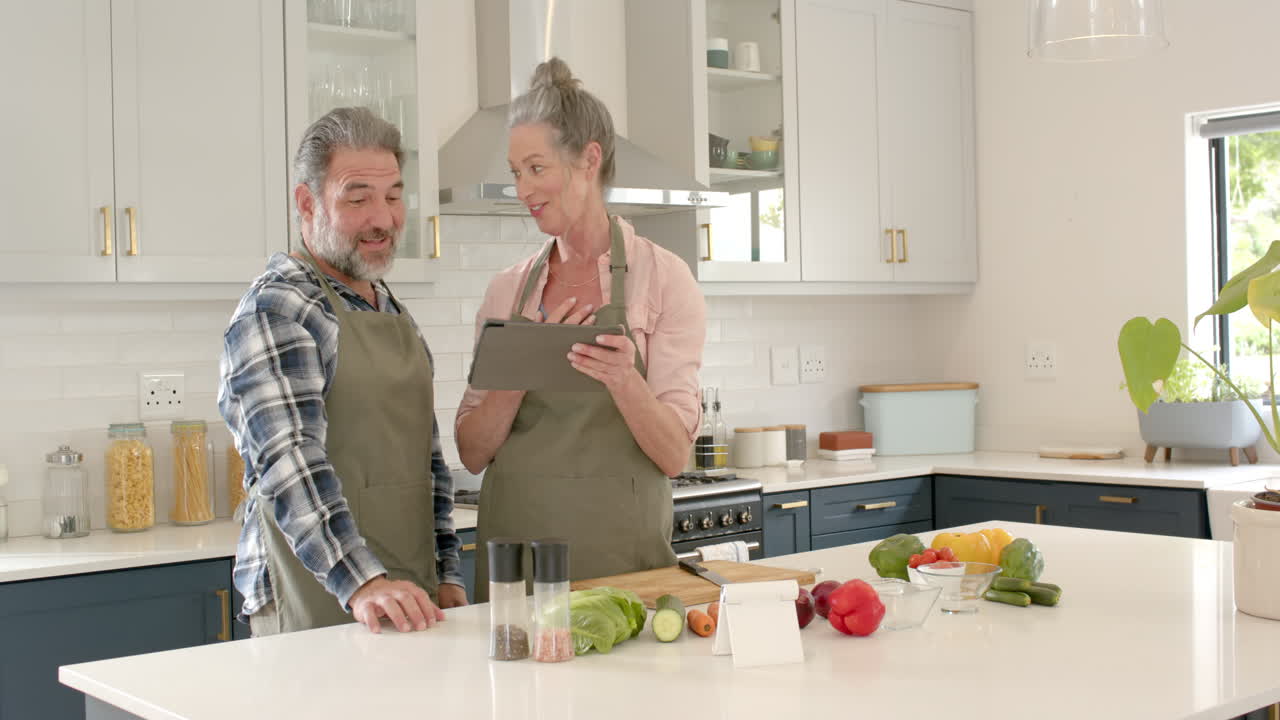Mature couple cooking together in kitchen, using tablet for recipe inspiration