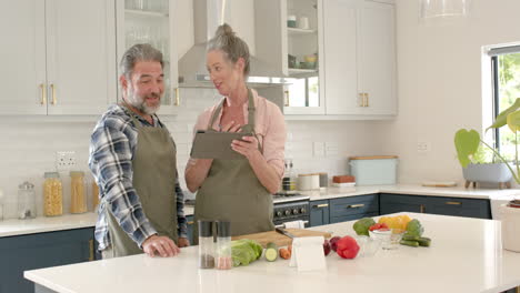 mature couple cooking together in kitchen, using tablet for recipe inspiration