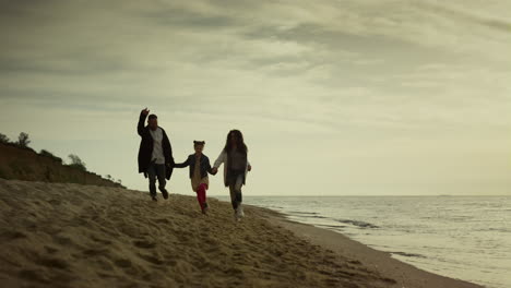 family hold hands beach by sunset sea. mom dad child running sand on holiday.