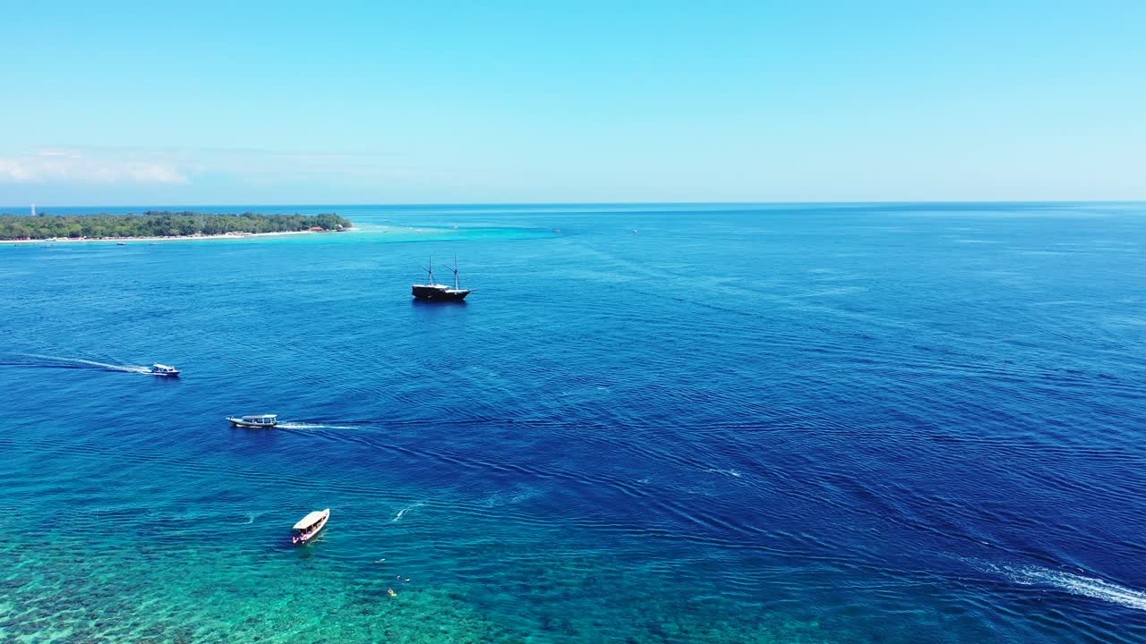 Small boats and a large ship sailing across the surface of beautiful blue waters off the coast of a tropical island