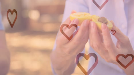 animación de corazones cayendo sobre familia caucásica comiendo frutas en el parque