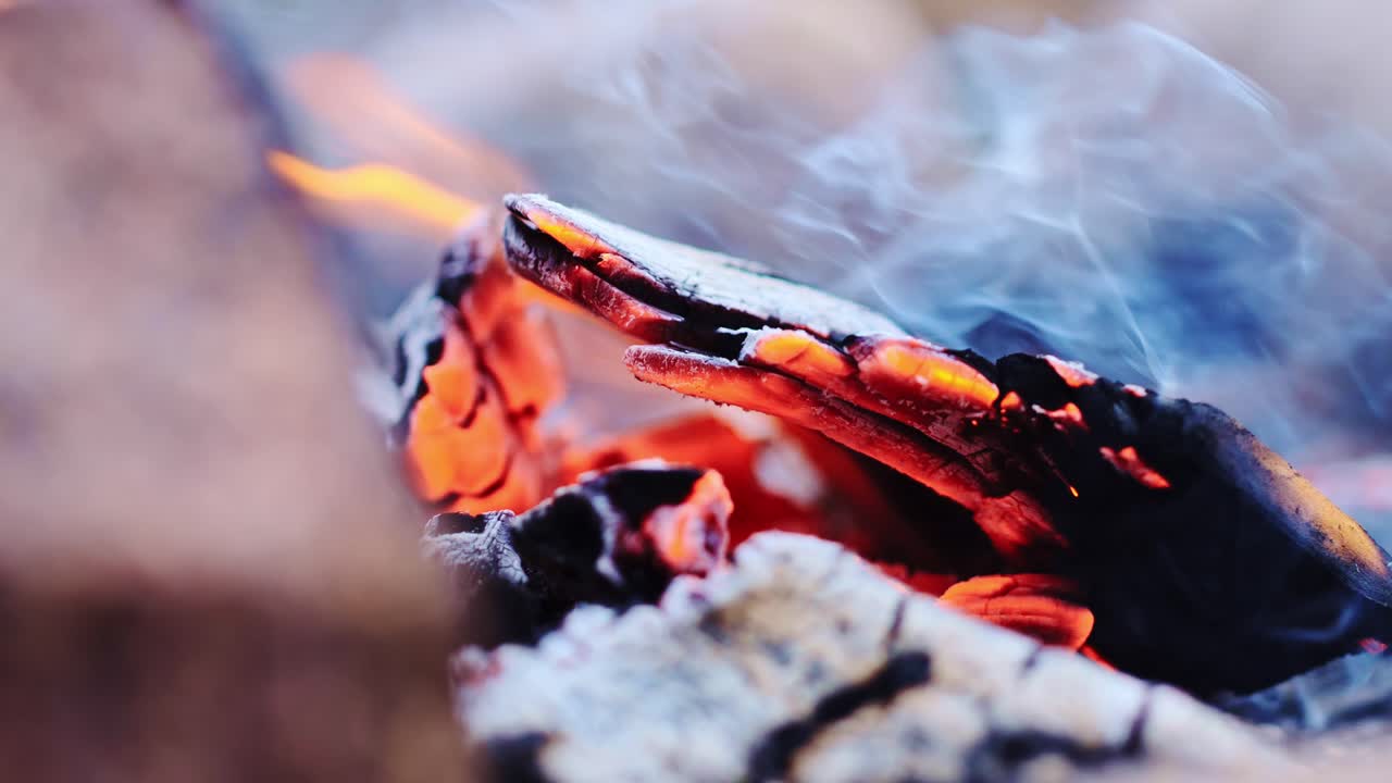 Close-up of a burning log glowing with intense orange heat, surrounded by ash