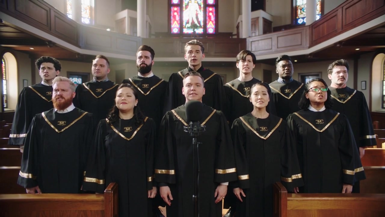 Coro che inizia a prendere fiato, cantando un inno in chiesa in tonache nere con finiture dorate, microfono.