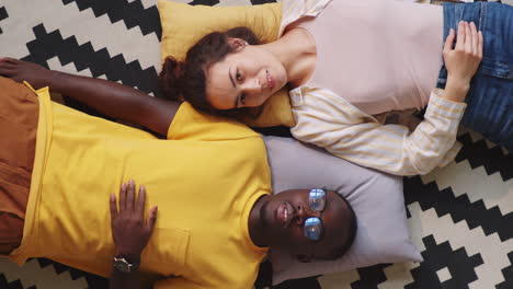 multiethnic couple lying on floor at home and posing for camera