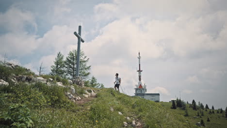 camera tracking backwards, hiker walking away from a radio tower on mountain uršlja gora, walking past a big cross