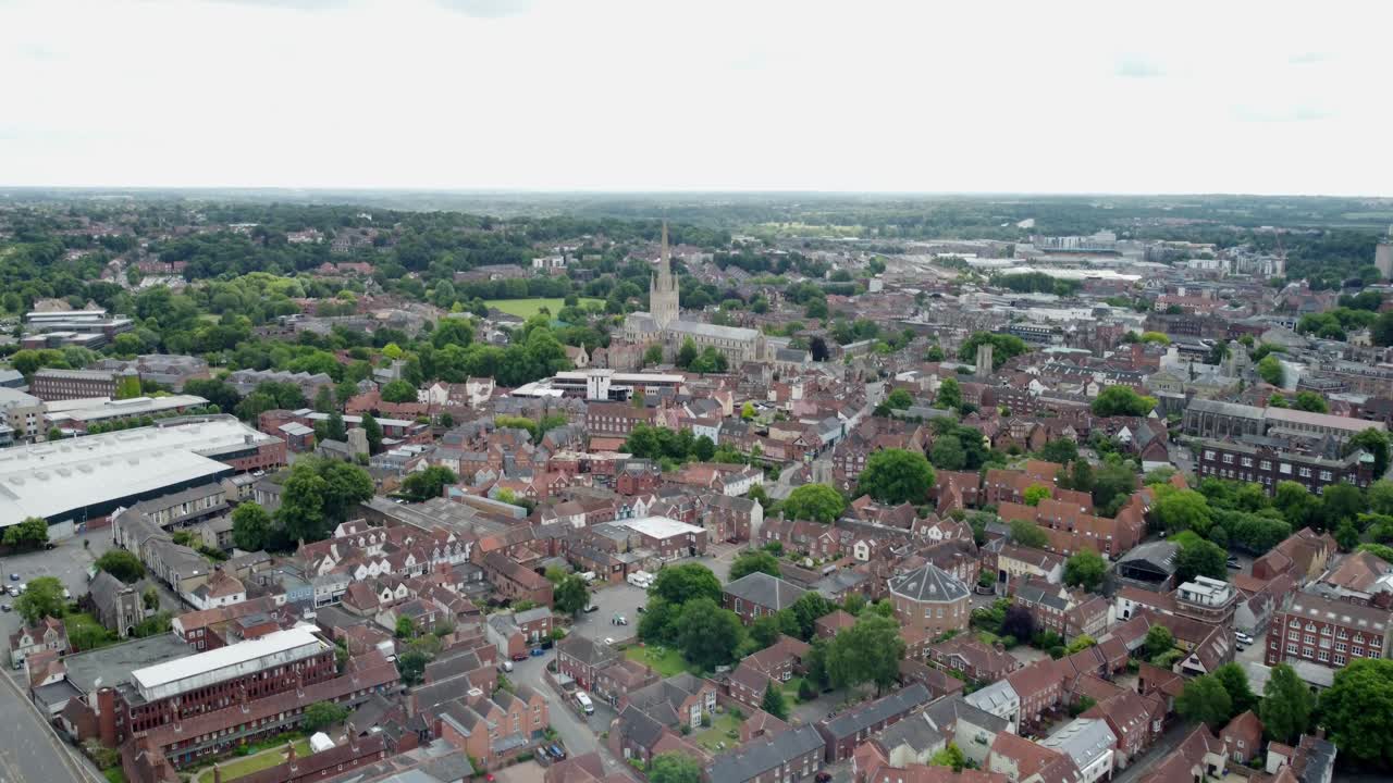 Aerial footage over Norwich City Centre. The footage moves to the left and pans up slowly. Shows the cities cathedral, commercial buildings, surrounding residential homes and green areas. Norfolk.