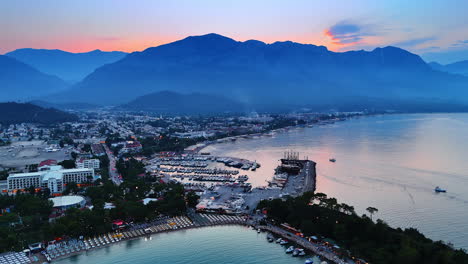 Beautiful resort city of turkey at sunset time. Drone flight over the beaches and yacht club. Mountain silhouettes at backdrop. Kemer, Turkey
