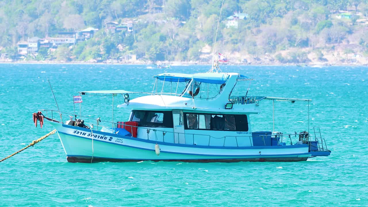 Stationary fishing boat in bright daylight, calm turquoise sea, distant shoreline, steady camera shot