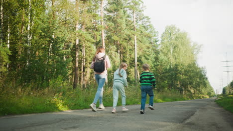 rear view of joyful siblings running playfully alongside their older sister on quiet paved road bordered by lush green forest, capturing carefree outdoor family bonding on a bright sunny day
