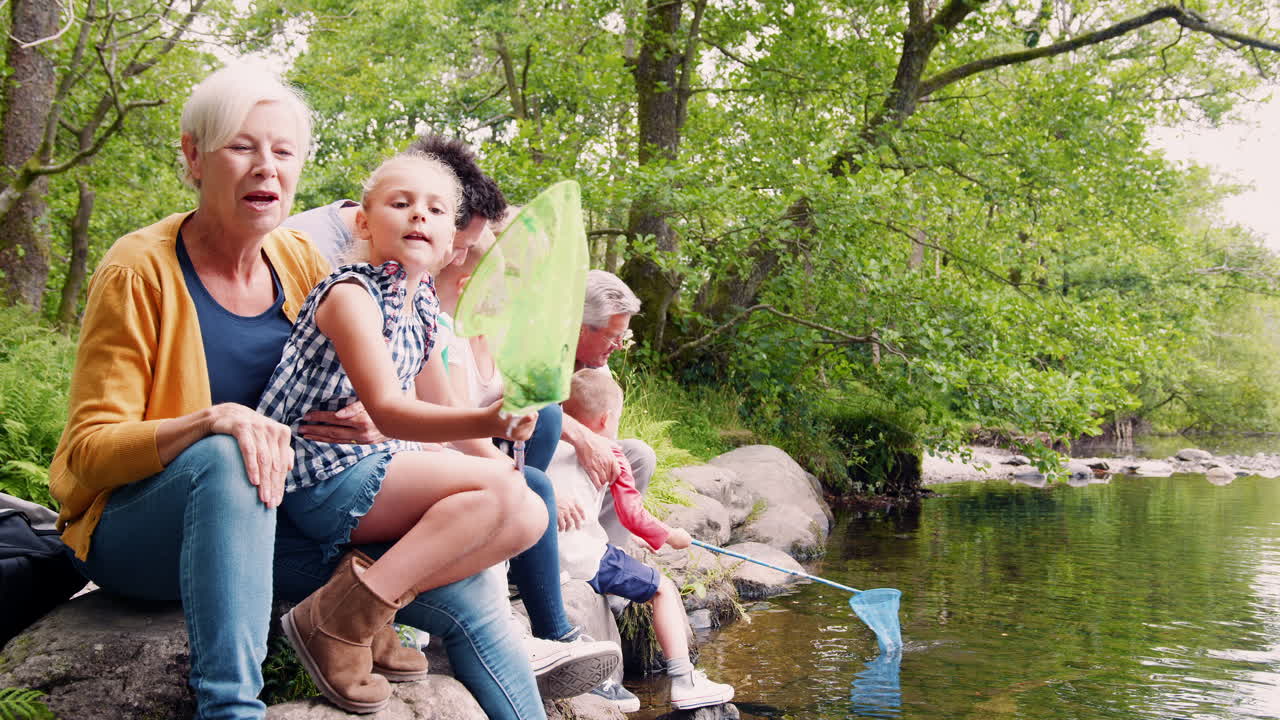 Slowmotion-optagelse af en flergenerationsfamilie, der sidder på klipper og fisker med net i en flod i den britiske Lake District