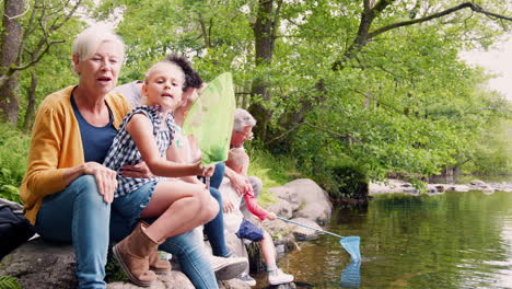 slow motion shot of multi generation family sitting on rocks fishing with nets in river in uk lake district