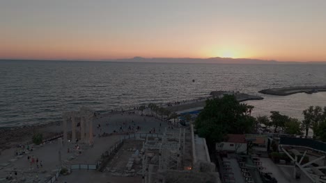 Seitlicher-Hafen,-Uferpromenade,-Luftaufnahme,-Sonnenuntergang,-Himmel-über-Der-Altstadt-Und-Den-Griechischen-Klassischen-Ruinen-Des-Apollon-Tempels