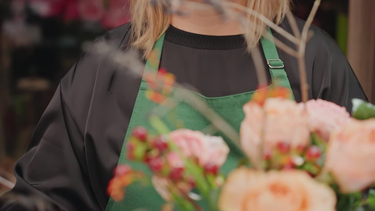 Fiorista caucasica che ispeziona un bouquet di rose finito, espressione calma e concentrata con primi piani su petali, bacche e accenti di rametti, delicato bilanciamento degli steli e stile finale per l'ordine del cliente, accogliente e calda