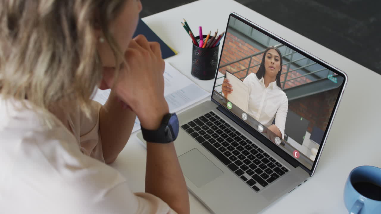 Empresaria caucásica usando una laptop para una videollamada con un colega de negocios birracial