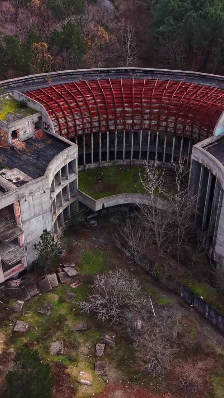 Aerial view of a circular abandoned structure with rusted roof