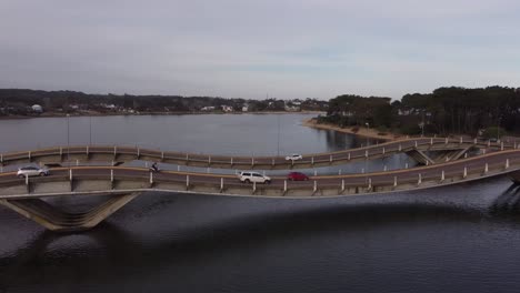 Drone-pov-of-Leonel-Viera-stressed-ribbon-bridge-with-vehicles-crossing-river-Maldonado-in-Uruguay