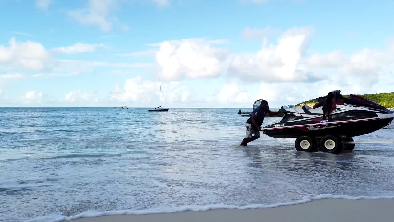 Three men pulling jet ski out of blue ocean with aid of waves