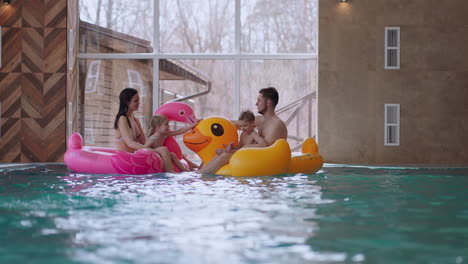 happy family in water park parents and children are floating on inflatable flamingo and duck and laughing