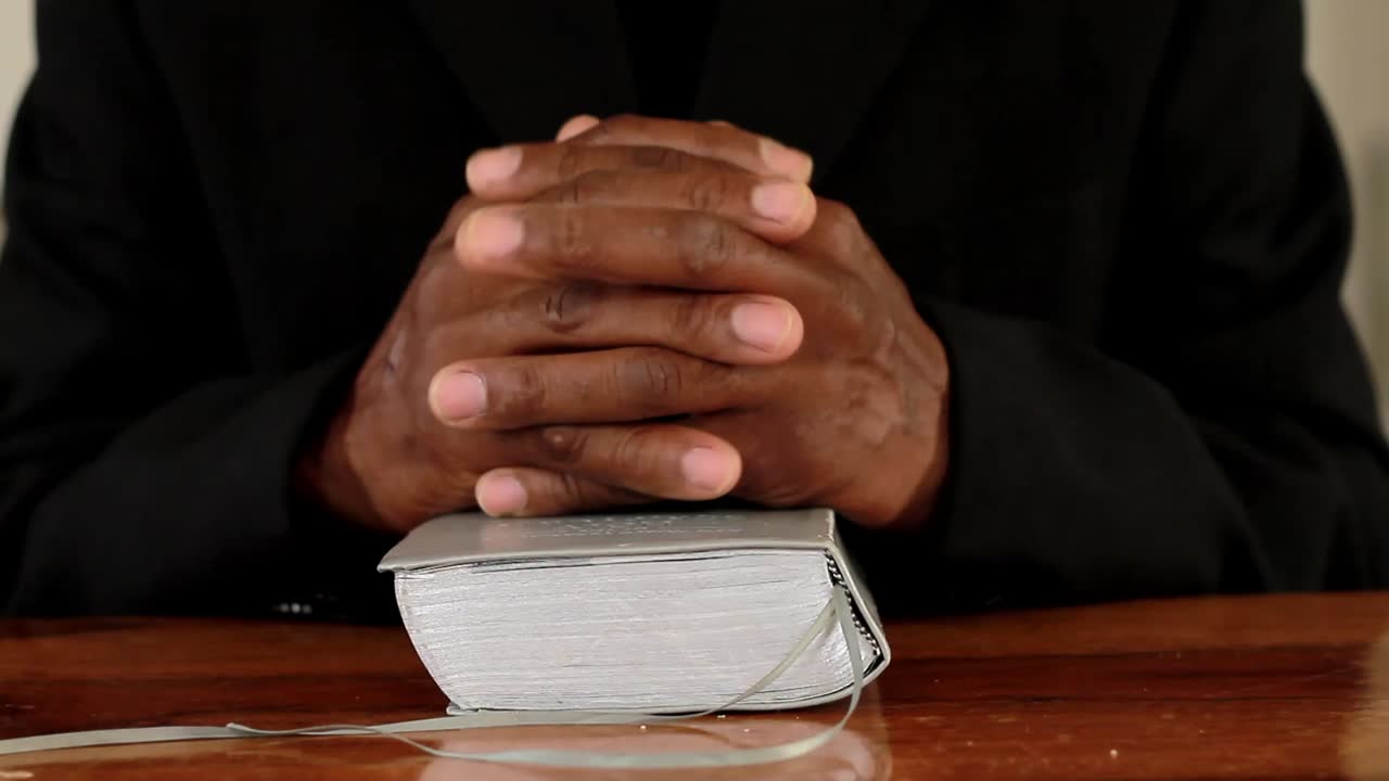 hombre rezando con la mano en el fondo negro de la biblia metrajes