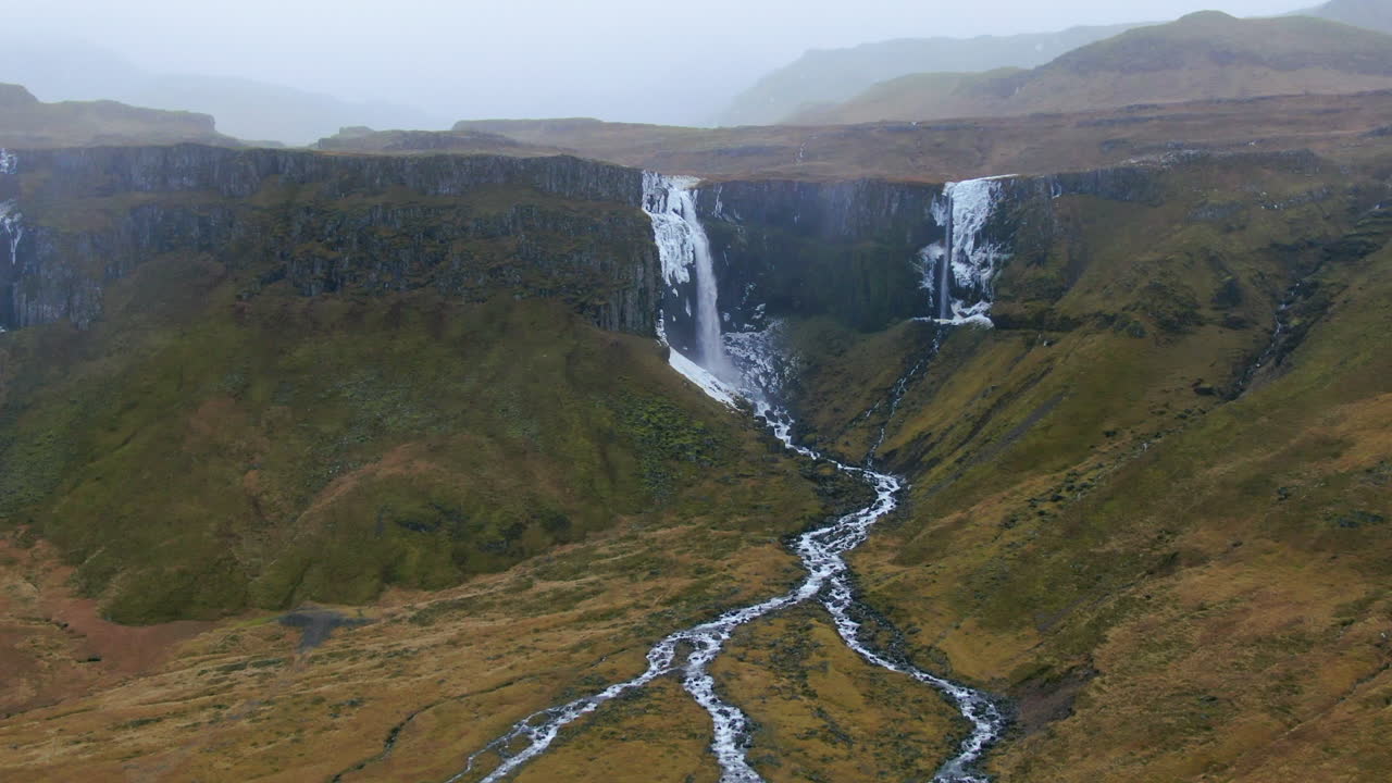 un avión no tripulado panorámica majestuosa cascada en cascada en un cañón y el agua fluye en diferentes arroyos en islandia kirkjufell montaña cerca de grundarfjordour