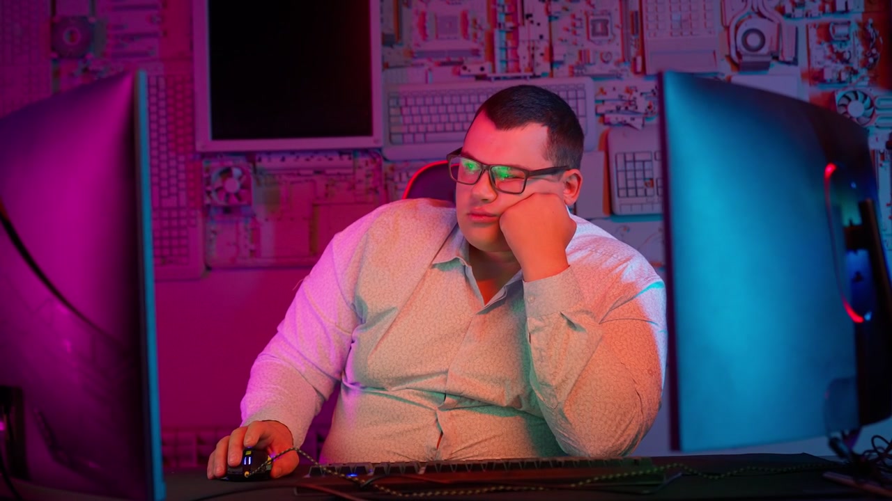 Bored Man Resting Head While Working on Computer with Neon Lights