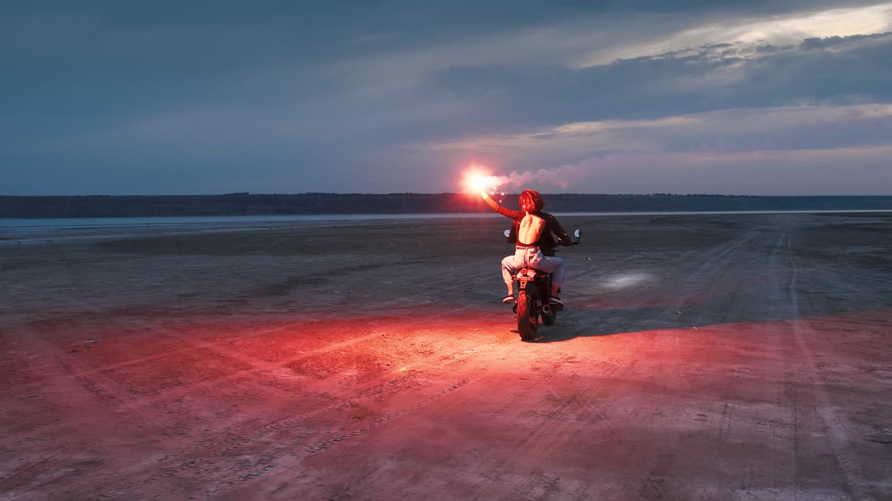 은 불타는 신호와 함께 빈티지 오토바이를 타고 있는 커플이 해변에서 일몰 후 불을 고 있다.