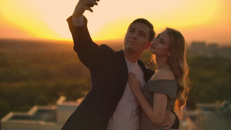 standing on the roof at sunset a married couple a man and a woman hug and take a selfie on the phone. take pictures of yourself standing on the roof and hug. young people in love