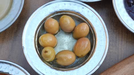 a close-up of green olives in a small silver bowl on a wooden table