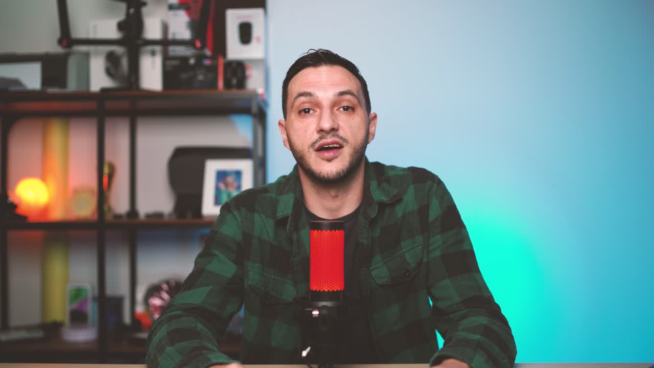Male vlogger sits in a home podcast studio, talking to the camera while using professional audio equipment and cozy lighting.