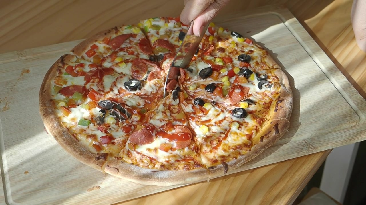 Ahşap tahta üzerinde taze pişmiş pizza kesen kişi.