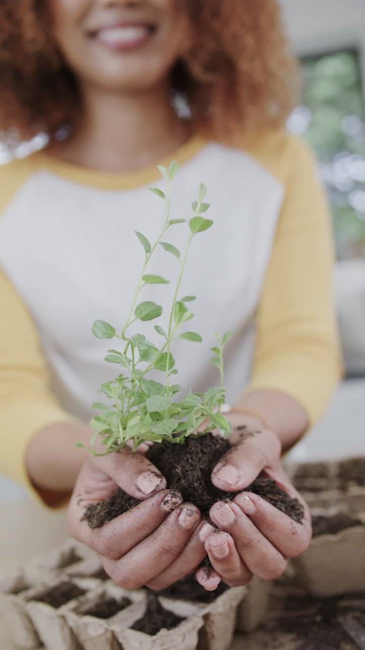 Vertical video of happy african american woman holding ground with plant in slow motion