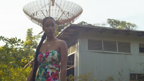 un modelo camina en primer plano con una torre de rastreo de radio abandonada al fondo en la isla de trinidad