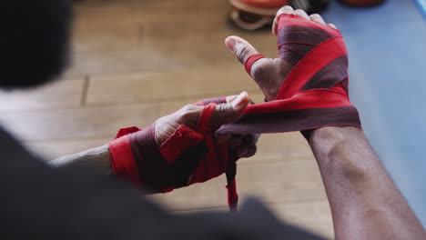 primer plano del entrenamiento del boxeador masculino en el gimnasio poniendo envolturas en las manos de pie junto al saco de boxeo