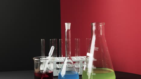 Coloured-liquids-in-flasks-with-test-tubes-in-stand-on-black-and-red-background,-slow-motion