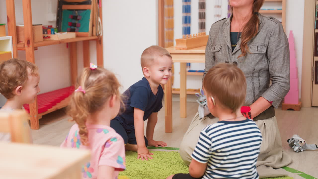 Betreuer, der Kleinkinder mit einer Spielzeughasenpuppe während einer spielerischen Aktivität im Klassenzimmer beschäftigt und Lachen, Fantasie und Lernen fördert, während die Kinder voller Neugier und Freude zusehen
