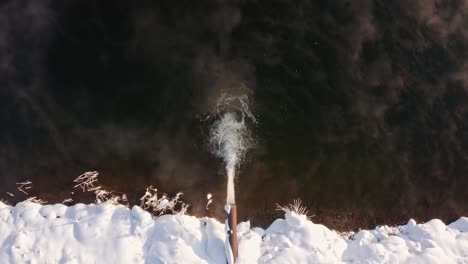 vista de arriba hacia abajo de la tubería de drenaje con agua corriendo en el lago durante el invierno en frydman, polonia