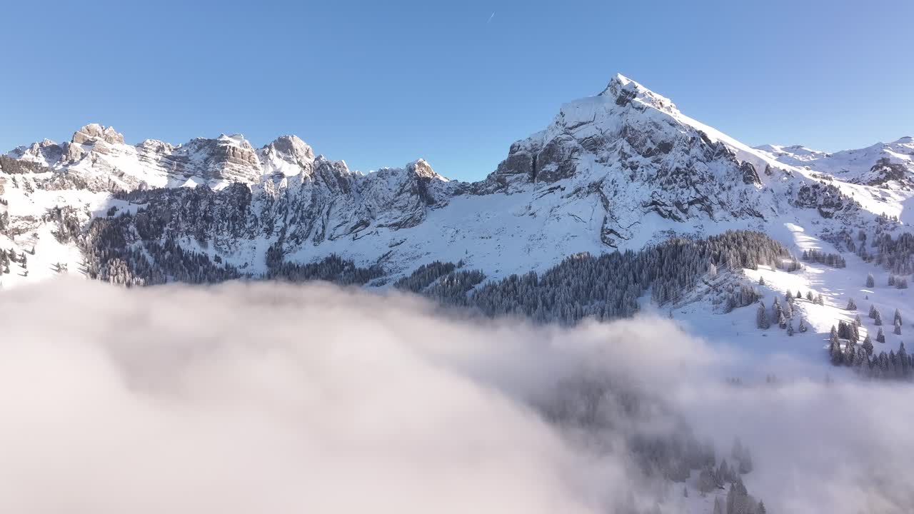 Fronalpstock innevato a Glarona, Svizzera, con nuvole e foresta alpina sottostante.