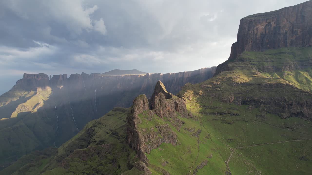 Aerial drone view of dramatic flat topped mountain and steep rocky peaks with green slopes and clouds casting shadows across wild landscape in Sierra de Guara during daytime