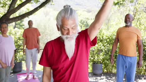 Diverse-senior-male-instructor-and-friends-practicing-yoga-standing-in-sunny-nature,-slow-motion