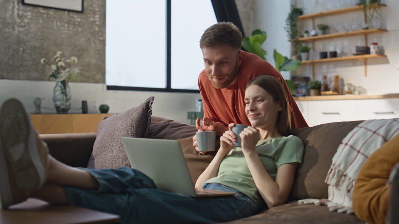 Home couple looking laptop at modern living room. Relaxed woman sitting sofa