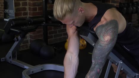 tattooed muscly man in home gym working out goblet bicep curl