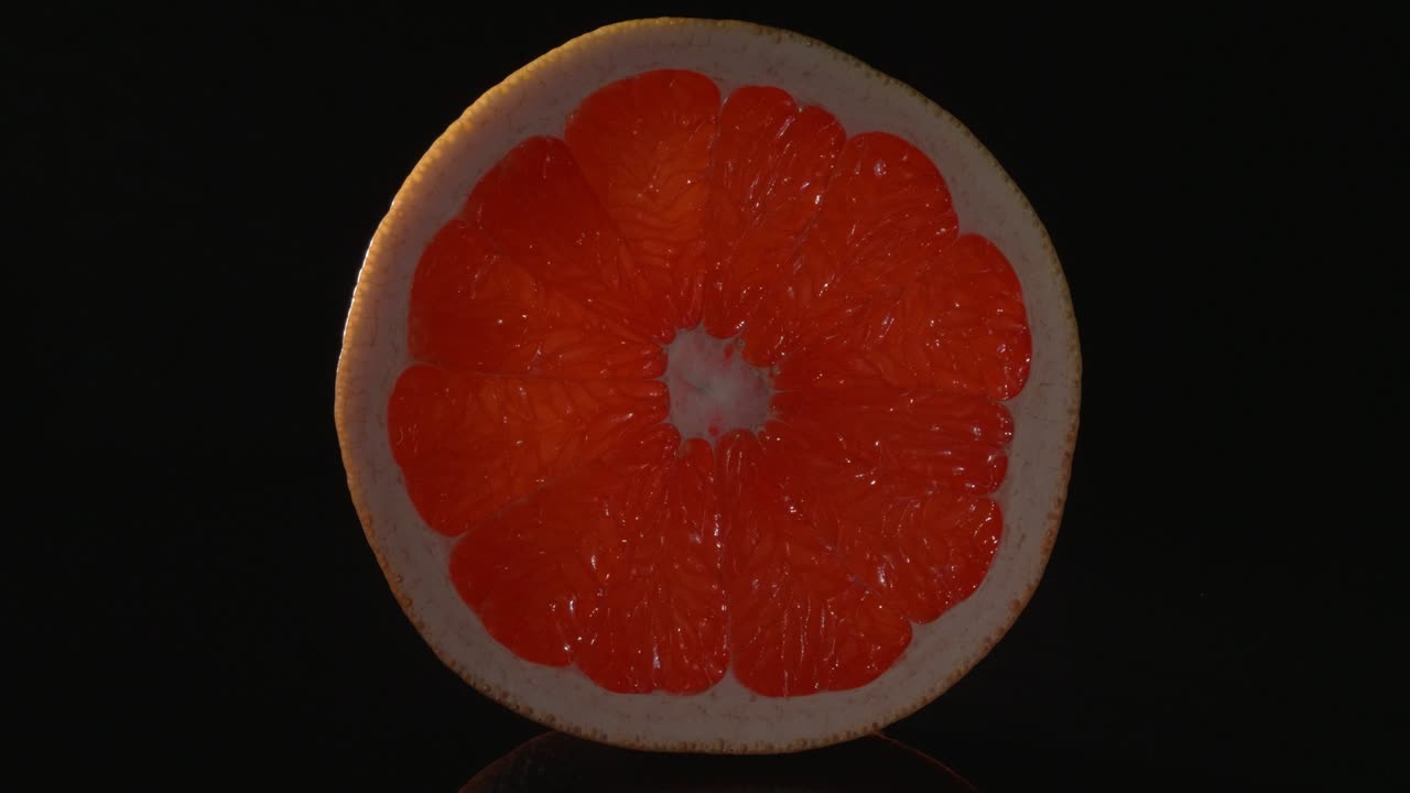 una rebanada redonda de pomelo en primer plano sobre un fondo negro.