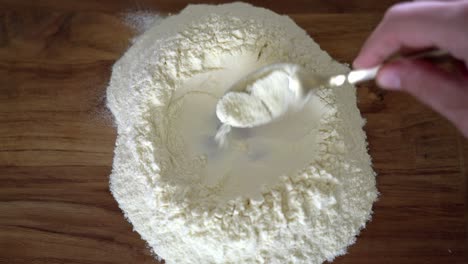 caucasian hand prepares a flour mould and pours water in it, making pasta