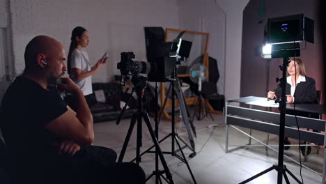 focused male photographer looks at the camera directed on the brunette caucasian woman. lady in white t-shirt stands at backdrop holding a phone. studio footage of a blog