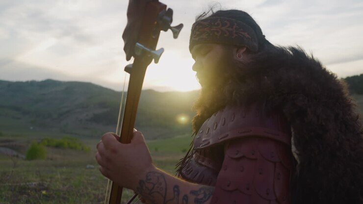 Plump musician plays igil with bow against mountain at dawn